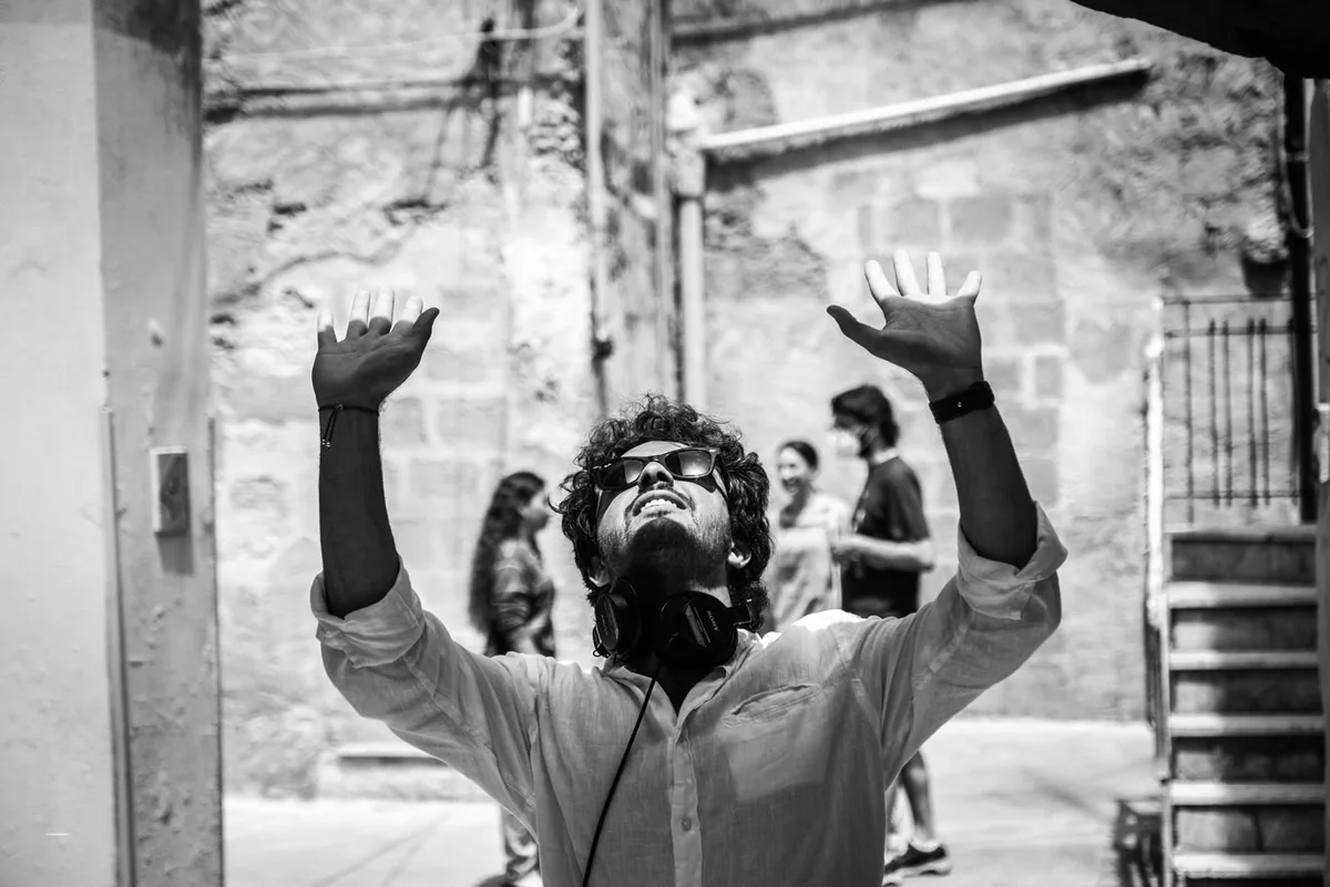 Fabio Schifilliti en rodaje en un callejón soleado, con auriculares al cuello y los dos brazos levantados.
