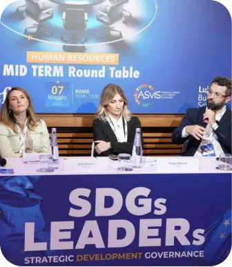 Four panellists behind a table on a blue-lit stage, the screen behind them reading SDGs Leaders — Mid Term Round Table.
