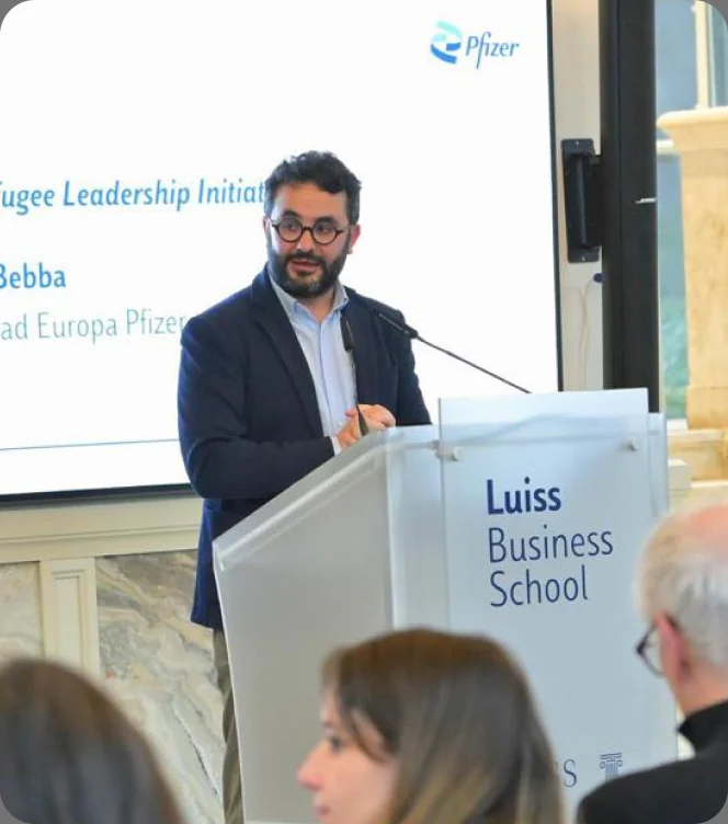 Antonio Bebba speaking from a lectern at Luiss Business School, a Pfizer slide on the screen behind him.