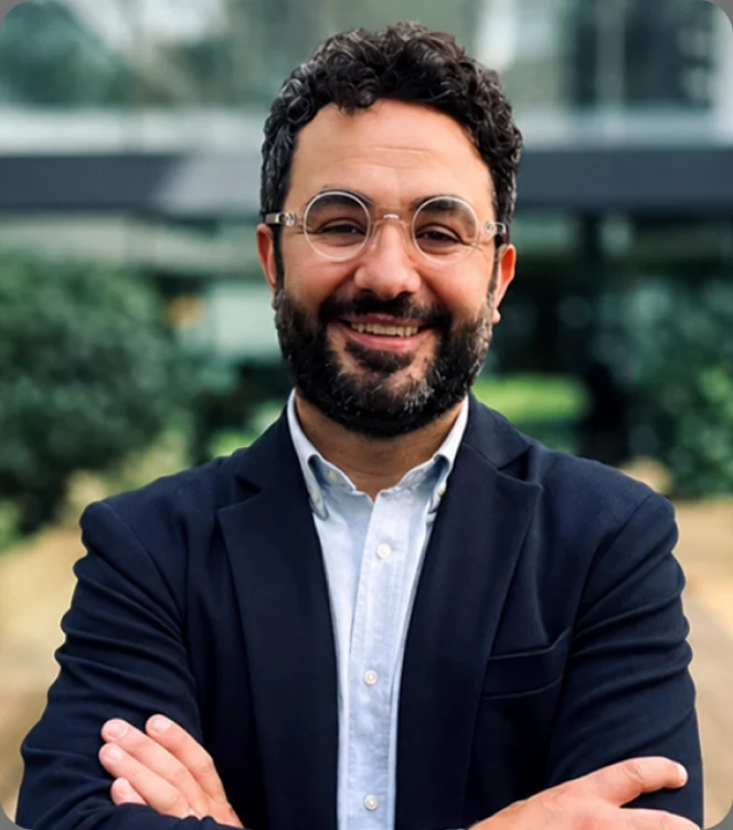 Antonio Bebba, arms folded, smiling, photographed outdoors in front of a glass building.